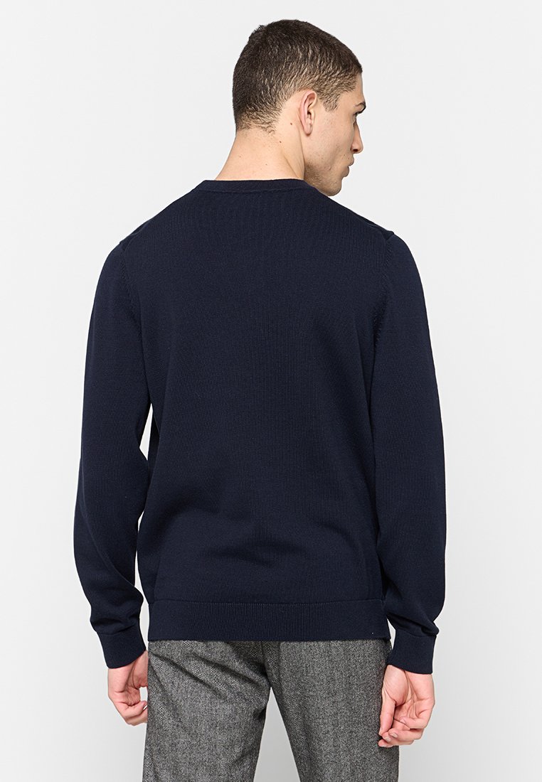 Pull en maille bleu marine à manches longues et poignets côtelés, avec un ourlet droit et un motif texturé. Vue de derrière affichée.