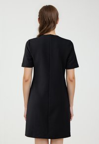 Robe noire à manches courtes avec une silhouette droite, dotée d'une couture centrale à l'arrière et d'une texture lisse. Design minimaliste.
