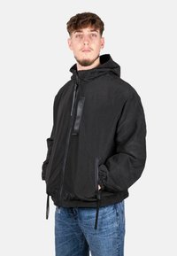 Giacca nera con zip in tessuto testurizzato, cappuccio regolabile e polsini elasticizzati. Presenta una tasca anteriore con zip e cordini all'orlo.
