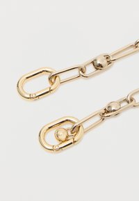 Corrente de metal dourado com elos ovais e acentos redondos. Acabamento suave com uma superfície refletora. Variações subtis nas formas dos elos.