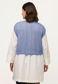 Ljusblå stickad kort vest med en lös nätdesign och ribbad fåll, bärs över en lång vit skjorta. Mjuk textur, korta ärmar.