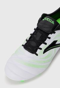 White soccer shoe with black laces and accents, featuring a textured design and green highlights. The brand logo appears on the tongue.