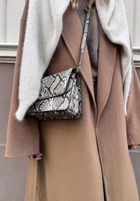 Crossbody bag in snake print with a black trim. Soft gray and brown overcoat with a light gray shawl. Smooth texture and rectangular shape.
