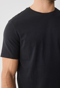 T-shirt de algodão preto com gola redonda e mangas curtas, textura suave e design ajustado. Simples, minimalista, sem padrões ou realces.