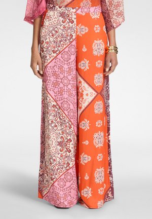 Mujer que lleva una falda de patchwork colorida que combina rosa, naranja, crema y granate con intrincados patrones florales y de paisley, y pulseras doradas en la muñeca derecha.