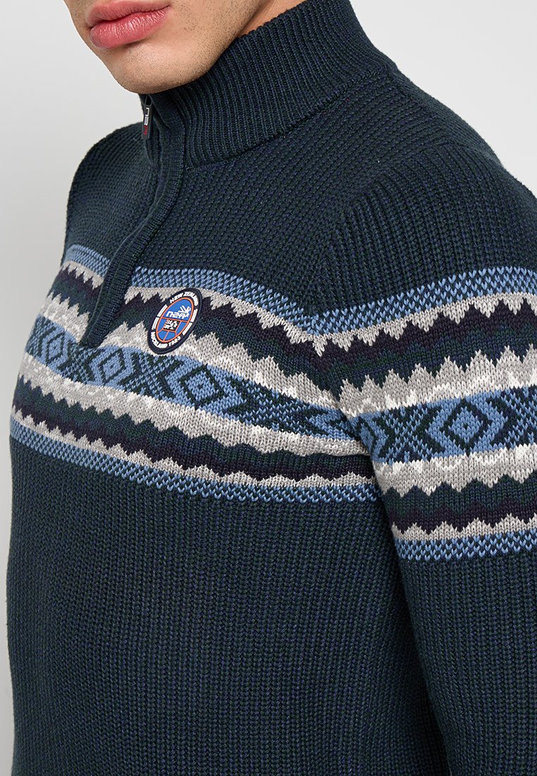 Donkerblauw gebreid sweater met een ritskraag, voorzien van een geometrisch patroon in lichtblauw, grijs en marineblauw over de borst.