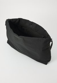 Black nylon bag with a soft, textured exterior, a zippered interior pocket, and cinched top, featuring a subtle embossed logo on the front.