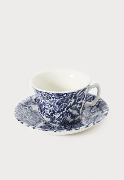 Conjunto de chávena e pires em cerâmica com padrões florais azuis intricados sobre fundo branco; chávena curvada com pega, textura lisa.