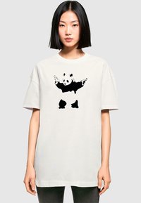 White oversized t-shirt featuring a graphic of a panda holding two guns. Short sleeves, round neckline, and a relaxed fit.