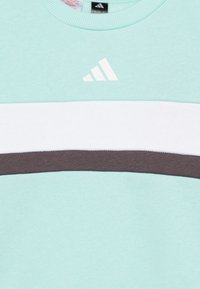 Sudadera azul claro con cuello redondo, que presenta una franja horizontal blanca y una franja marrón debajo. Contiene un logo blanco en el pecho.