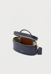 Temno modra usnjena torbica z zadrgo, zgornjim ročajem in zlato okovjem. Notranjost ima kontrasten rjav kartični držalo. Gladek tekstura.