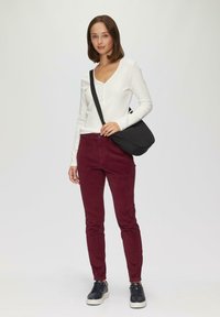 Langärmliges weißes Rippoberteil mit V-Ausschnitt, kombiniert mit burgunderfarbenen Slim-Fit-Hosen und schwarzen Sneakers. Enthält eine schwarze Umhängetasche.