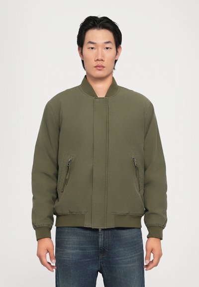 Chaqueta bomber verde oliva con un cuello alto, bolsillos laterales con cremallera, puños elásticos y un ajuste relajado. Textura de tela suave.