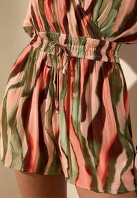 Primer plano de un mono con cinturón en la cintura con rayas abstractas verdes, rosas y rojas sobre tela ligera y texturizada.