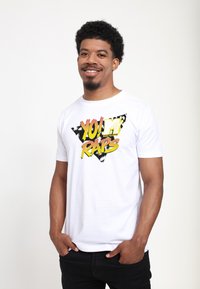 Hvid cotton t-shirt med et sort og gult grafisk trekantdesign og teksten "YO! MTV RAPS". Korte ærmer, standard pasform.