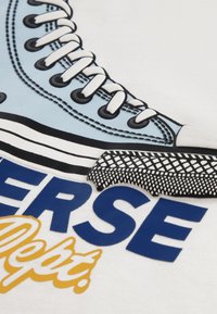 Σχεδίαση αθλητικού παπουτσιού σε ανοιχτό μπλε με μαύρες λεπτομέρειες, διαθέτει λευκά κορδόνια και υφή στη σόλα. Το κείμενο γράφει "Converse Dept." με έντονα γράμματα.