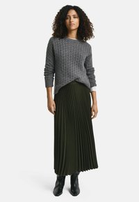 Grauer Kabelstrickpullover mit langen Ärmeln, kombiniert mit einem plissierten olivgrünen Maxirock und schwarzen Knöchelstiefeln.