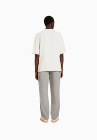 Volno střihnuté krémové tričko s krátkými rukávy ve spojení s volnými světle šedými cargo kalhotami s bočními kapsami a zúženými nohavicemi.
