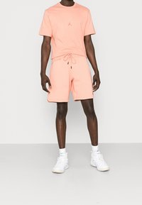 Camiseta de algodón rosa claro con un pequeño logo en el pecho, combinada con pantalones cortos a juego con cintura elástica y cordón.