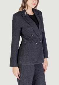 Blazer grigio scuro a spina di pesce con design doppiopetto, rever a punta e bottoni argentati lucidi. Vestibilità sartoriale con tessuto testurizzato.
