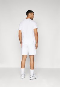 Hvid t-shirt og shorts outfit, som har korte ærmer, en rund halsudskæring og blød tekstur. Barbert med hvide sokker og sneakers.