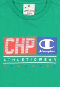Camiseta de algodón verde con el atrevido logotipo rojo "CHP" y el logotipo azul "Champion", acompañado del texto blanco "ATHLETICWEAR" y estrellas multicolores debajo.
