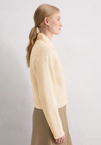 Hellgelber, fein gerippter Strickcardigan mit Kragen und Knopfverschluss, ausgestattet mit langen Ärmeln und einer verkürzten Silhouette.