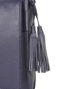 Námořnická kožená kabelka přes rameno s texturovaným povrchem, plochým tvarem a dvěma dlouhými třásněmi připevněnými k táhlu zipu.