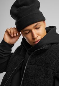 Čierna fleecová čiapka a prešívaná vesta cez čiernu mikinu. Fleece textúra na veste, s hladkým povrchom na mikine.