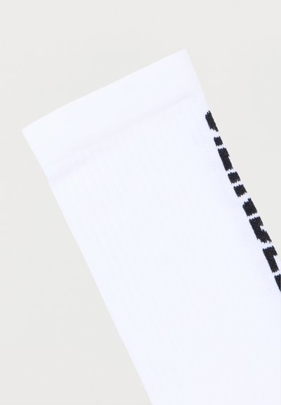 Άσπρη ριμπ ύφανση κάλτσα με μαύρο κείμενο στο πλάι, σε κοντινή λήψη πάνω σε απλό ανοιχτόχρωμο φόντο.