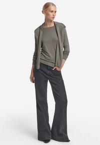 Hellgraues Longsleeve-Oberteil mit Kapuze, kombiniert mit dunklen, weitem Jeans. Glatte Stoffstruktur mit gerippten Bündchen und Saum. Schlichtes Design.
