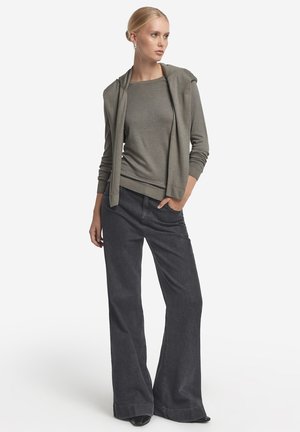 Ljusgrå långärmad tröja med huva, matchad med mörka vida jeans. Slät tygtextur med ribbade muddar och nederkant. Enkelt design.