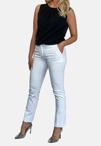 Mustat hihattomat toppi, jossa on laskostettu kaula-aukko, yhdistetty tiukkoihin valkoisiin housuihin ja kuvioituihin korkokenkiin. Taustatietoja ei ole.