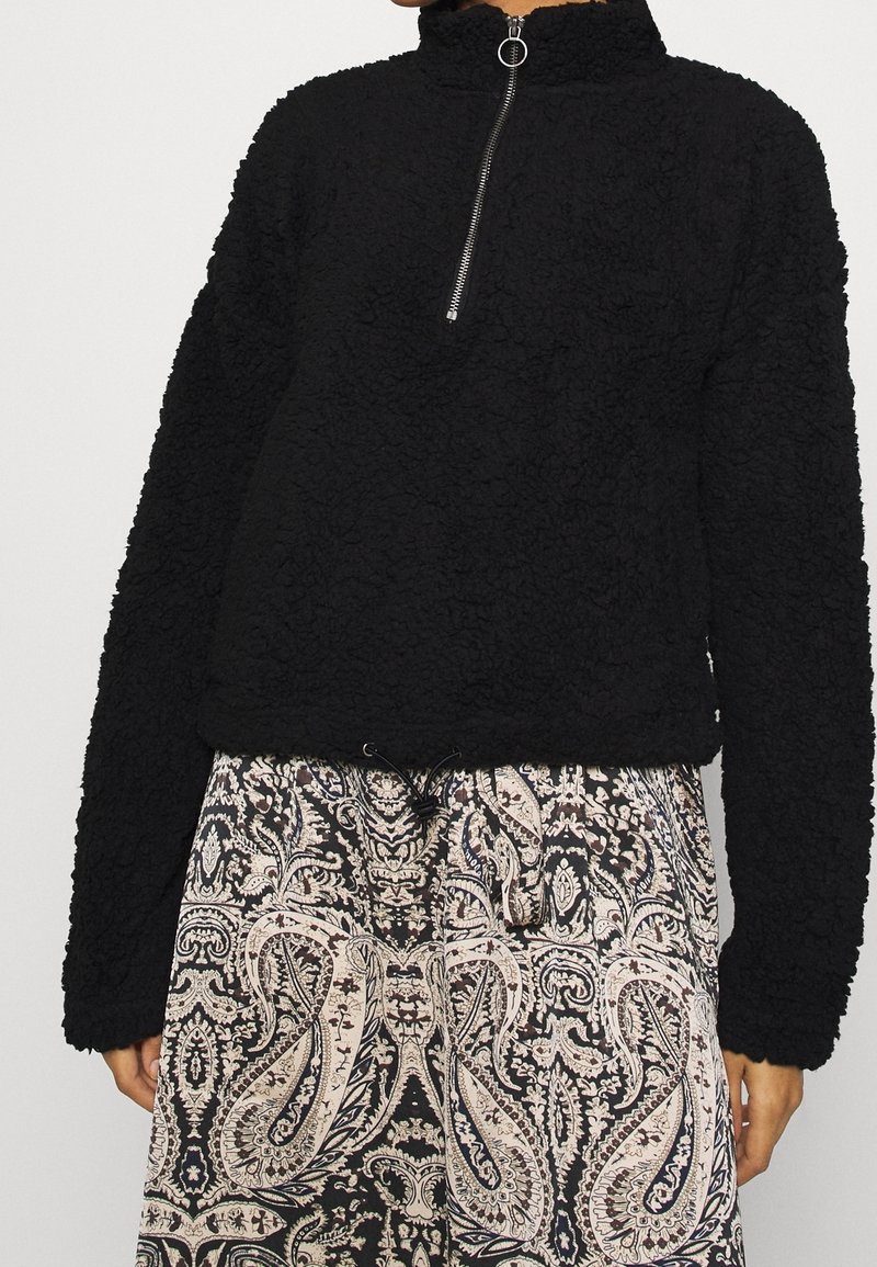Zwarte fleece pullover met hoge kraag en rits tot de helft. Kenmerkt zich door textiel met structuur, lange mouwen en een cropped ontwerp.