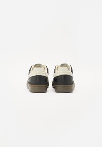 Baskets noires et crème avec une tige en cuir texturé, une semelle en caoutchouc, un col rembourré et un design minimaliste. Les accents comprennent des coutures contrastées.
