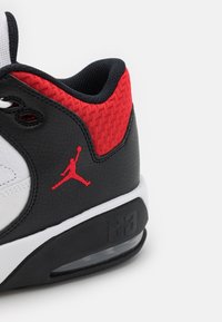 Białe i czarne sneakersy z czerwonymi akcentami, teksturowana cholewka, czarna skóra, poduszki powietrzne i czerwone logo Jumpman po boku.