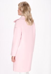 Šviesiai rožinė striukė su lygiu paviršiumi, turinti stovinčią apykaklę ir ilgomis rankovėmis. Dizainas yra iki kelių ilgio, su minimaliais akcentais.