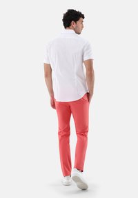 Weißes Kurzarmhemd mit dezentem Muster, kombiniert mit korallenfarbener Hose und weißen Sneakers, von hinten betrachtet.