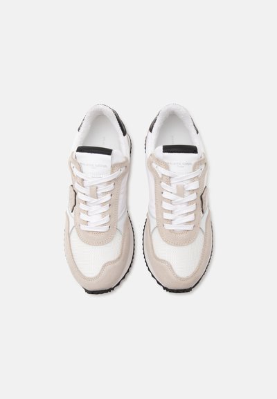 Paire de baskets blanches et beiges à lacets avec semelles noires et détails en mesh, vues de dessus sur un fond clair.
