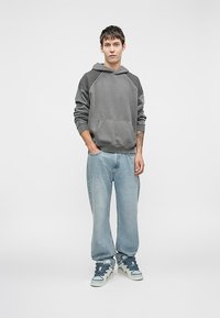 Gray hooded sweatshirt with a front pocket, paired with light blue loose-fit jeans and gray sneakers. Casual style with contrasting accents.