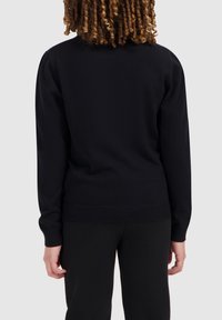 Zwarte trui met lange mouwen en geribbelde boorden, met een eenvoudig ontwerp en een nauwsluitende pasvorm. Draag met zwarte broek, waarbij de achterkant te zien is.