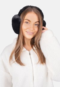 Cache-oreilles en fausse fourrure noire de forme ronde, à la texture douce et à l'ajustement confortable, portés par une personne vêtue d'une veste en polaire blanche.