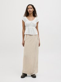 Witte peplum blouse met frills aan de mouwen, gecombineerd met een beige wikkel maxi rok. Model draagt zwart enkellaarsjes. Licht, gestructureerde stof.