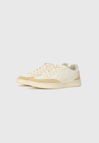 Baskets en toile crème avec des accents en cuir suédé beige clair, bout rond, détails perforés sur les côtés et lacets plats. Semelle en caoutchouc pour une meilleure adhérence.