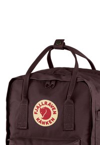 Sac à dos Fjällräven Kanken marron foncé avec deux poignées supérieures, une fermeture éclair et un patch logo circulaire représentant la silhouette d'un renard rouge.