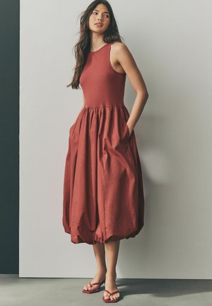 Bordeaux sleeveless dress with a fitted bodice and a voluminous, gathered skirt. Includes pockets and features a hem that cinches at the bottom.