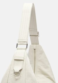 Cinghia di stoffa bianca con dettagli di cucitura, hardware in metallo, e una tasca con zip, caratterizzata da una texture liscia e un design minimalista.