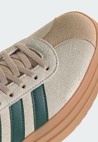 Sneaker in suede beige con strisce in pelle verde, tomaia in morbido tessuto, dettagli in color cuoio e suola in gomma leggera. Lacci di un colore neutro.