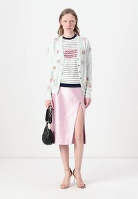 Cardigan azul claro con bordado floral sobre una camiseta a rayas. Falda metálica rosa con una abertura lateral. Un bolso negro y tacones nude completan el look.