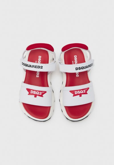 Sandales blanches avec accents rouges, dotées de deux brides ajustables portant l'inscription "DSQUARED2", d'une semelle intérieure rembourrée et d'une semelle extérieure noire texturée.